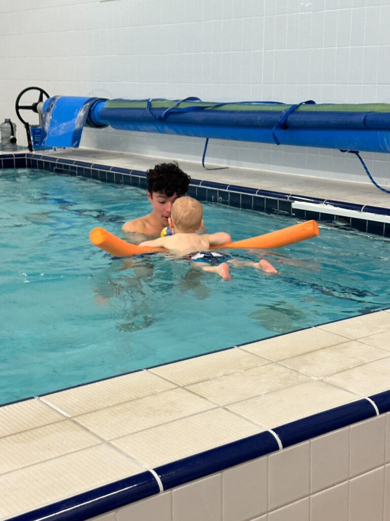 brothers in water babies lesson on pool noodle chasing a ball