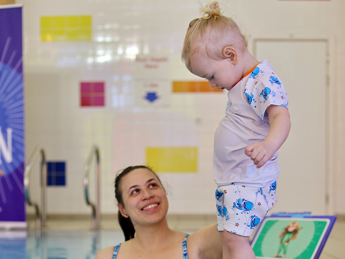 toddler standing on the edge of the pool in a water babies lesson