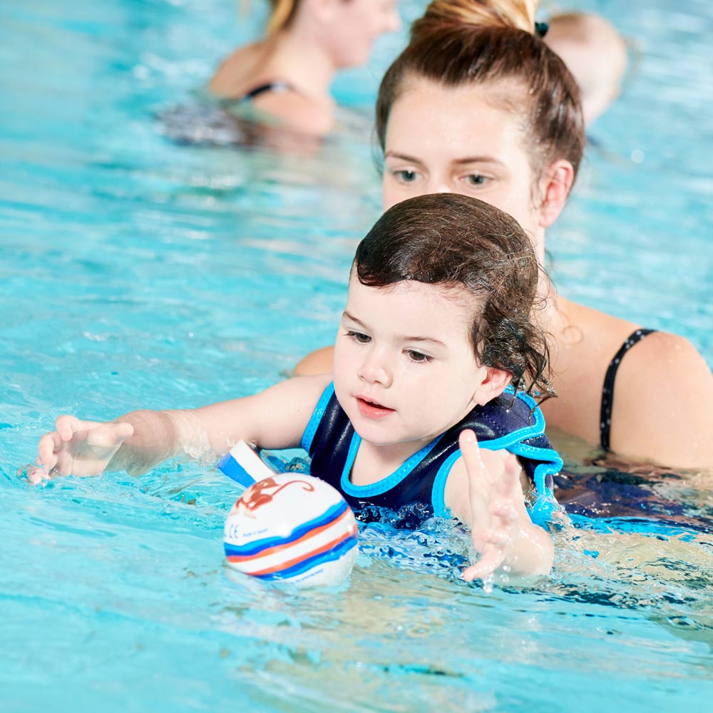 baby and mum in the pool chasing a swim ball