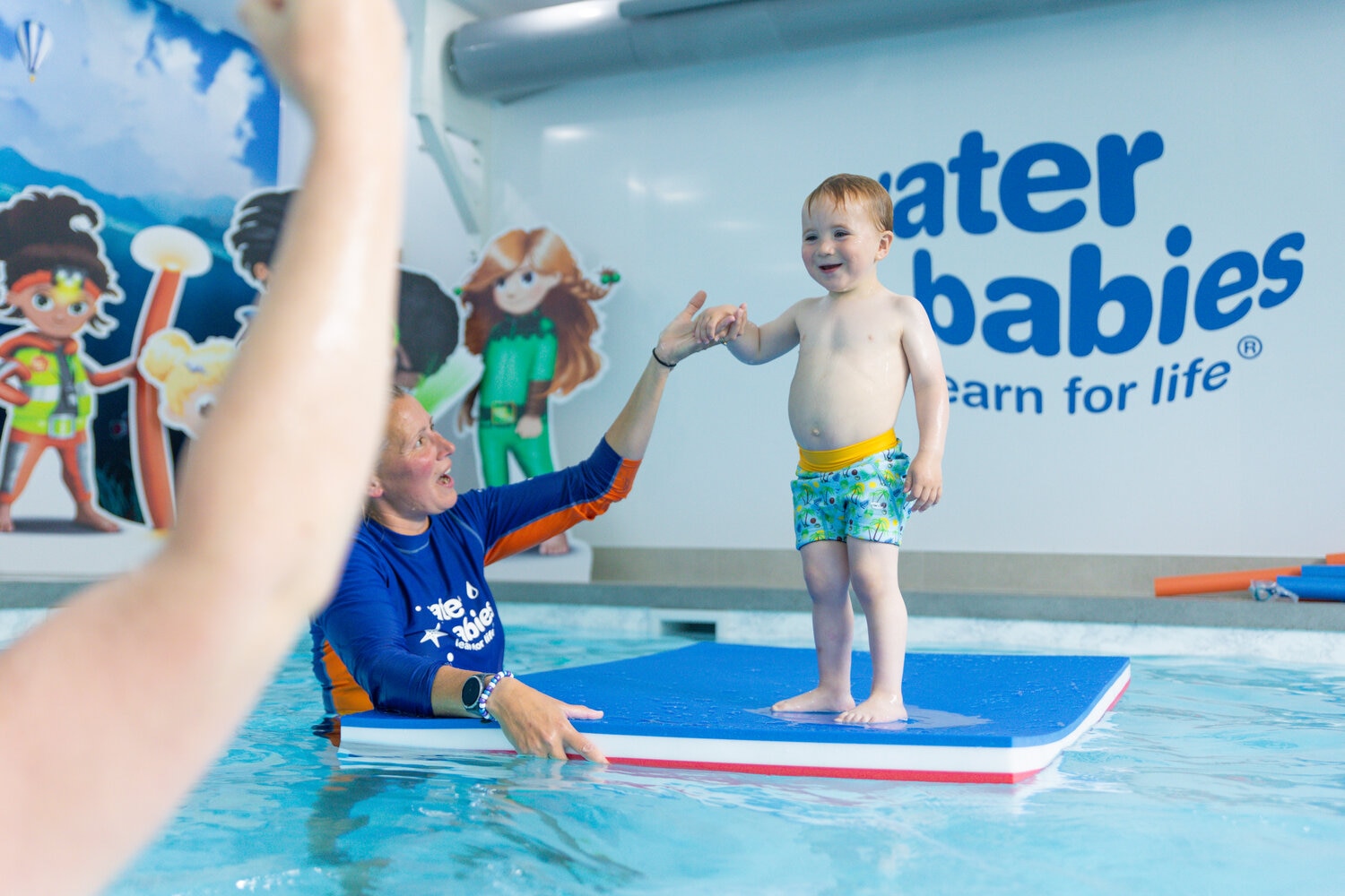 water babies toddler with parent standing on the mat in swimming pool
